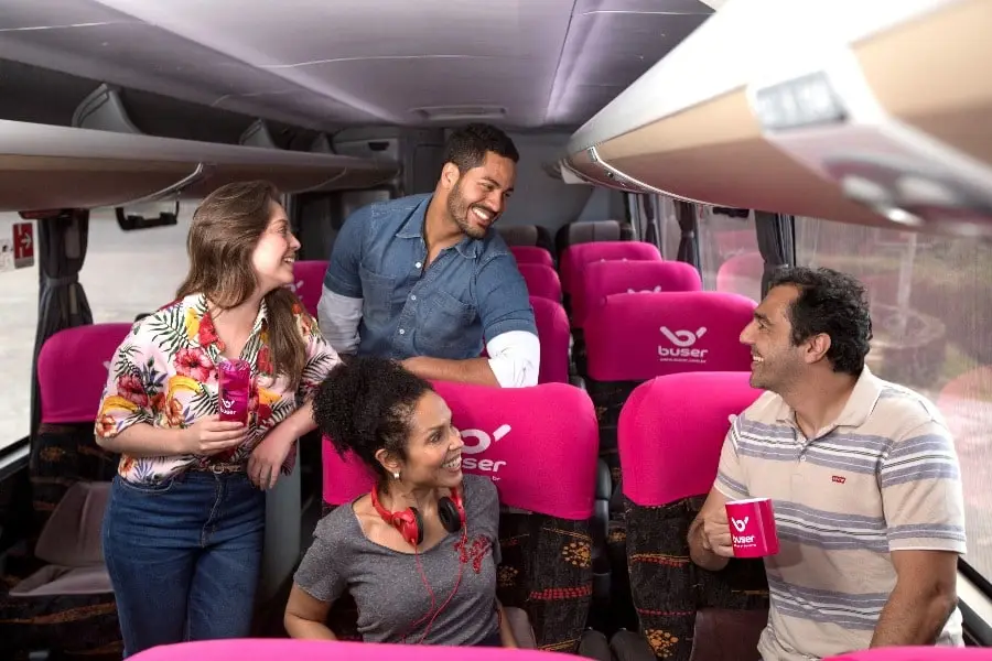 quatro pessoas alegres de gêneros diferentes mostrando na imagem o que é a Buser e como viajar