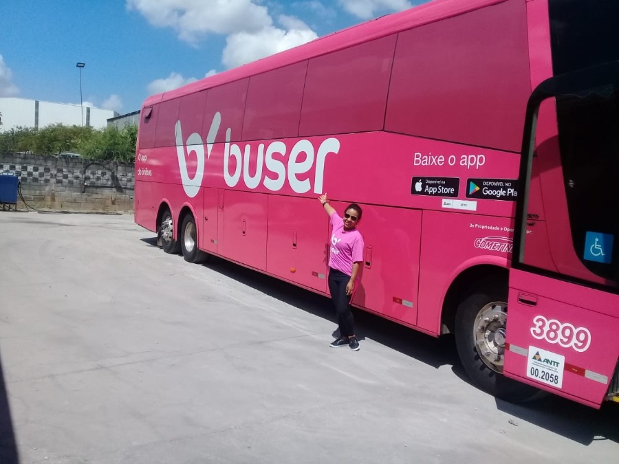 Júnia, mulher motorista de ônibus em frente a um ônibus da Buser