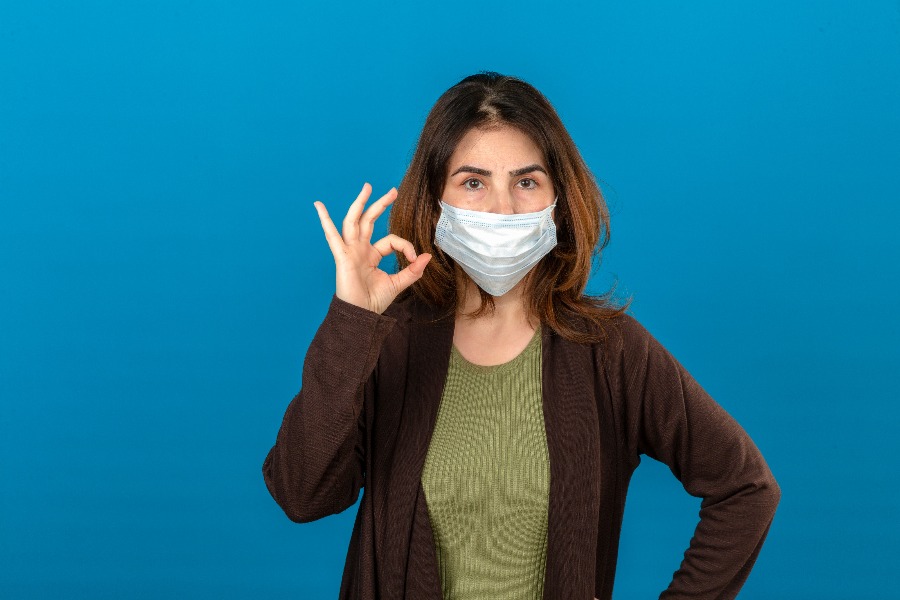 na imagem uma mulher branca usa uma máscara cirúrgica contra o coronavírus, indicando o jeito certo de usar a máscara em viagens.